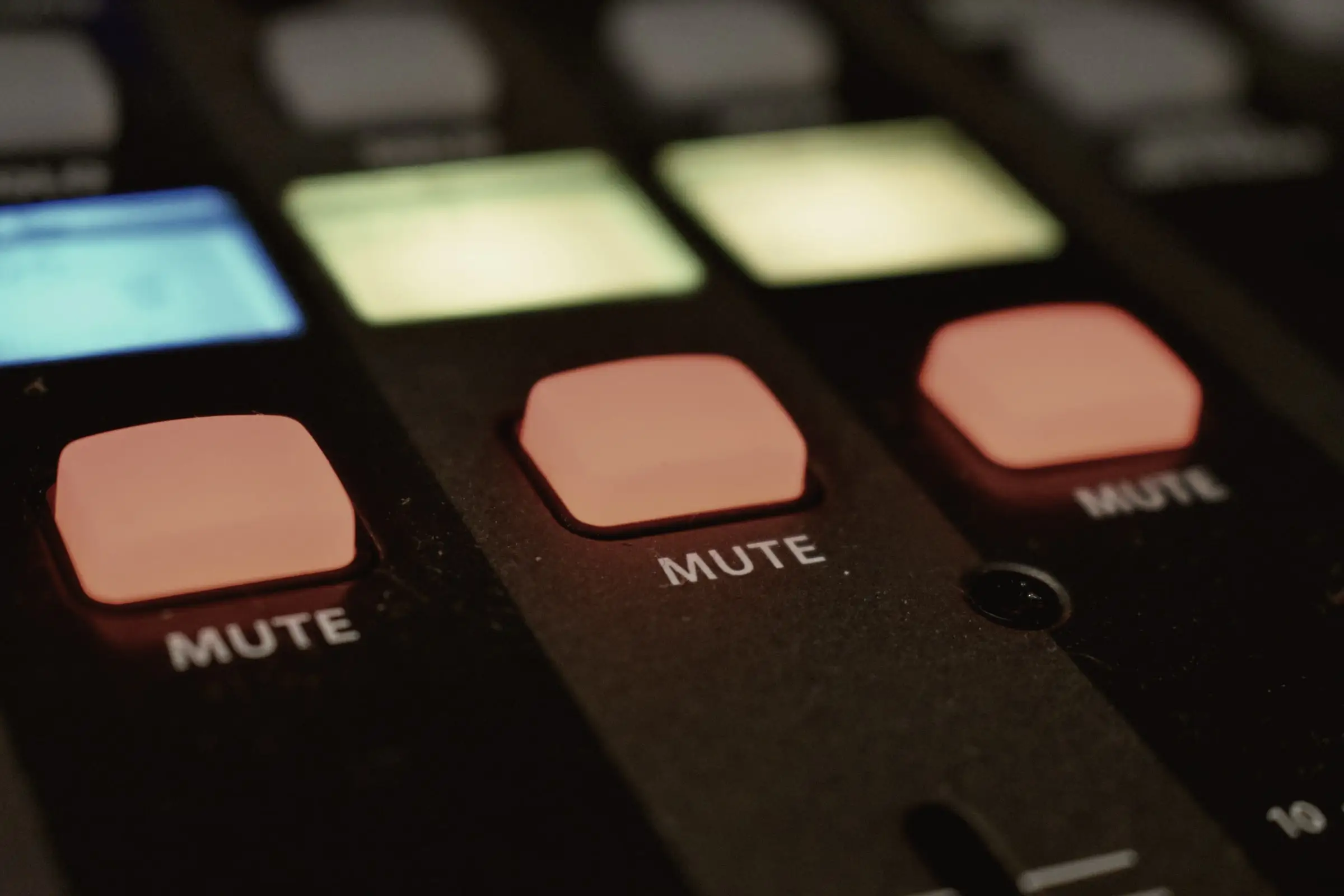 Close-up of glowing orange MUTE buttons and coloured pads on a mixing desk