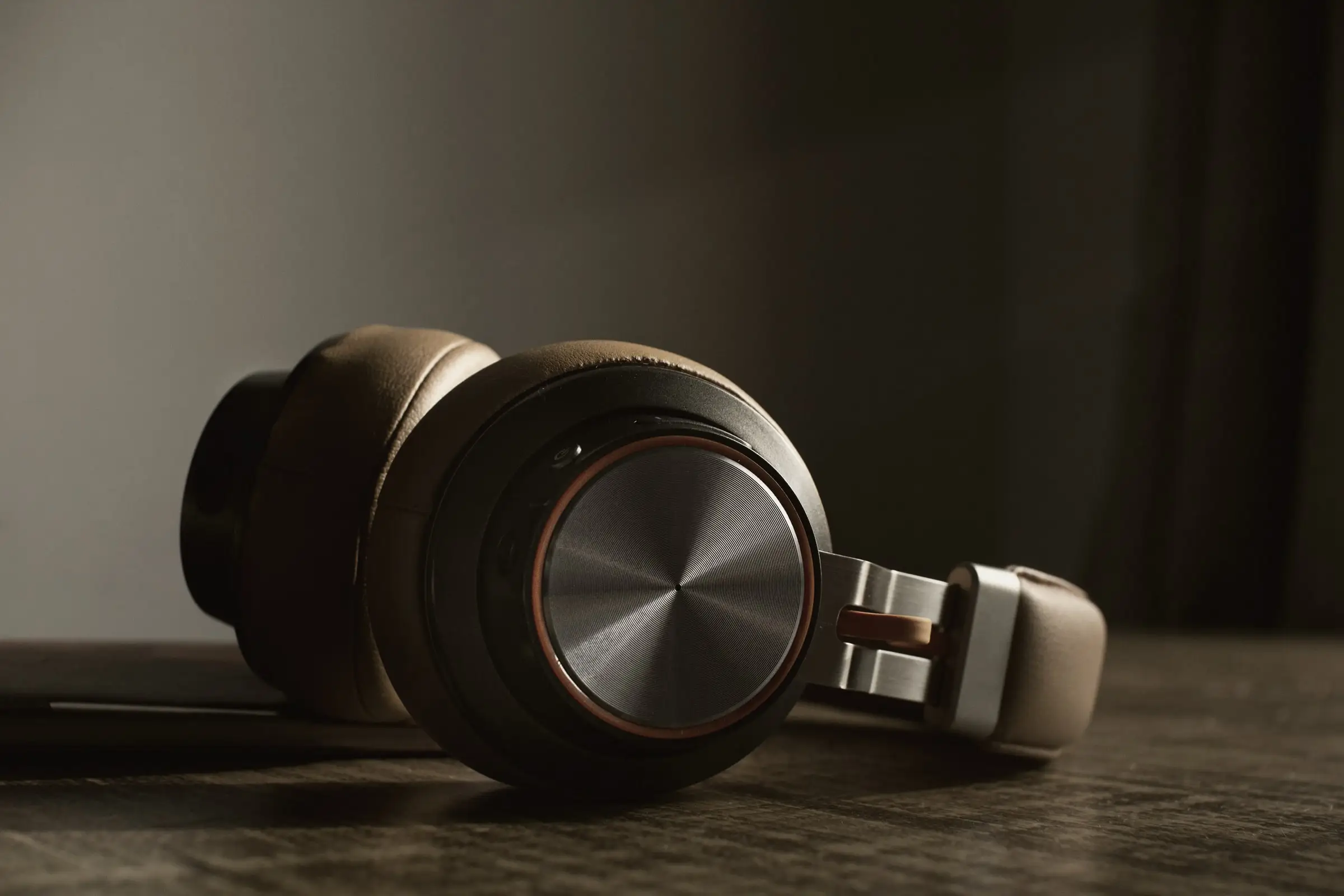 Over-ear headphones with brushed metal cup lying on a wooden table, dark wall behind