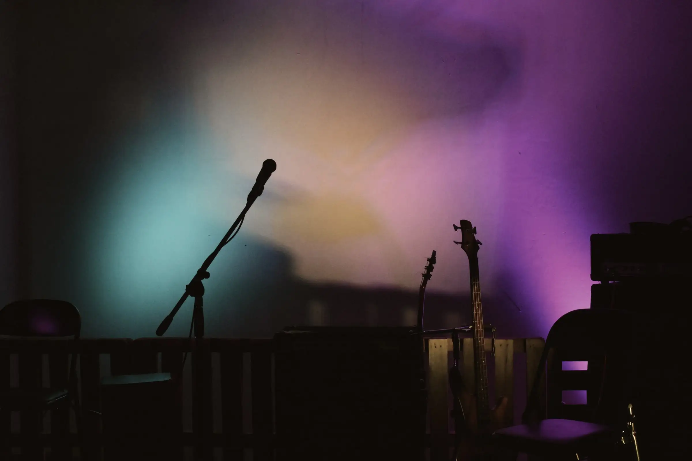 Empty stage silhouettes: mic stand and guitars against a blurred psychedelic teal, orange and purple wash