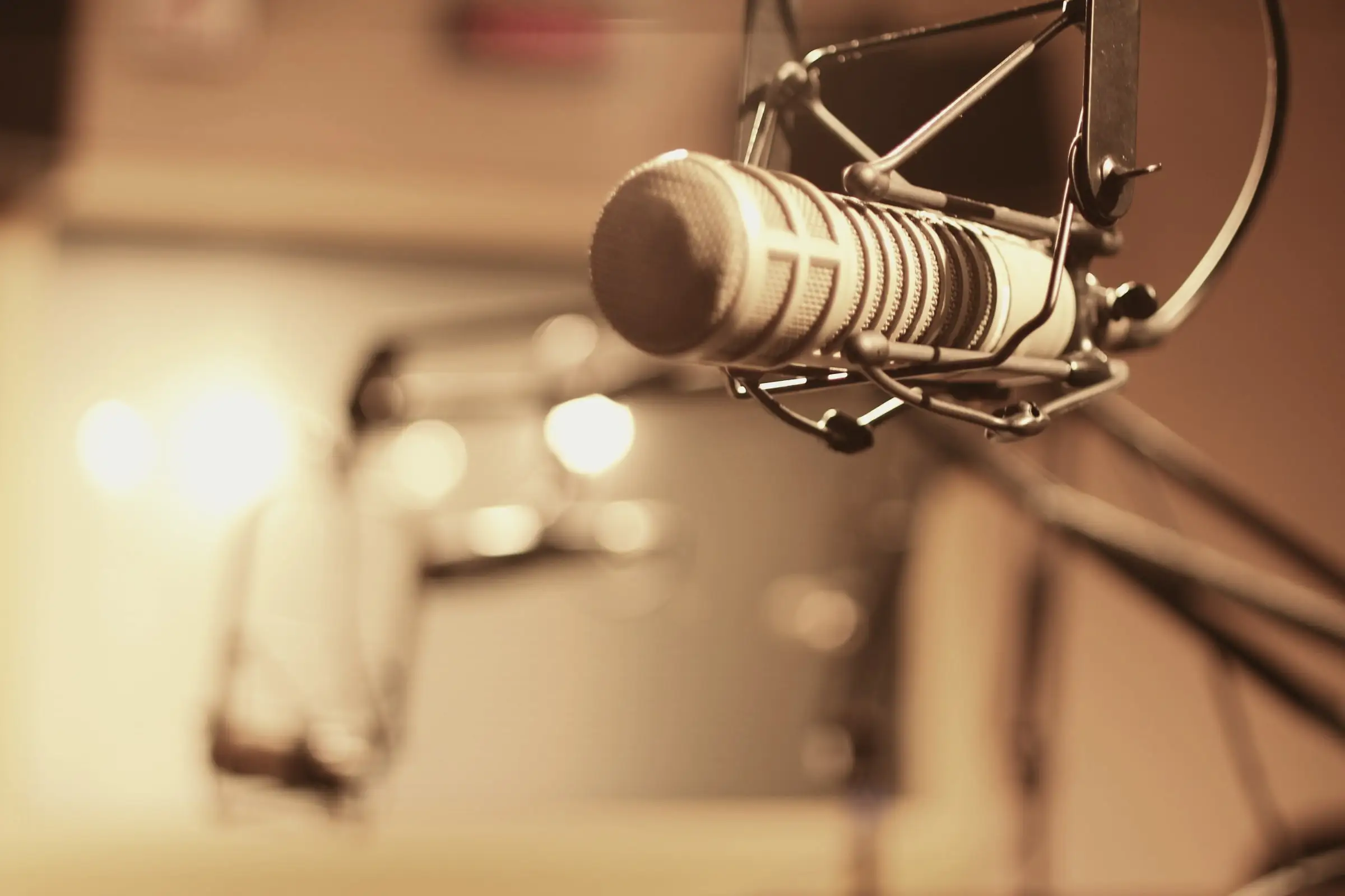 Broadcast-style vintage microphone in a shock mount, glowing in warm amber studio light with bokeh